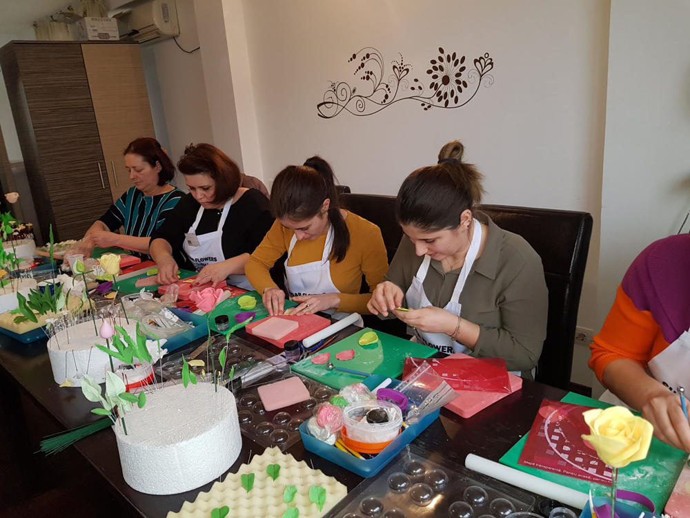 Femei care modeleaza flori comestibile din pasta de zahar, stand la masa.